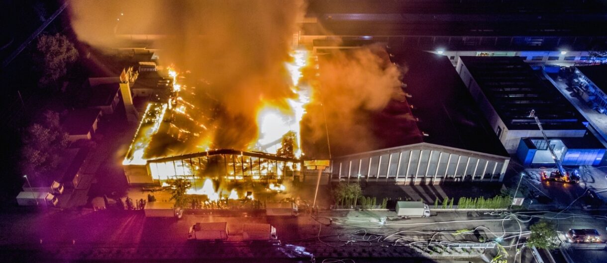 Aerial view of an industrial building engulfed in flames at night