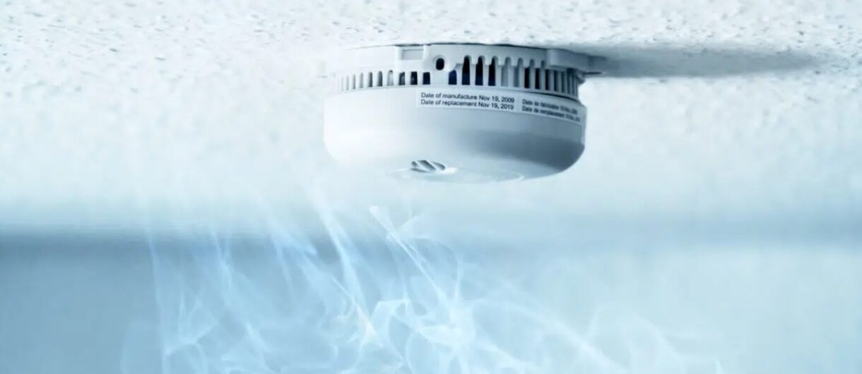 Smoke rising toward a ceiling-mounted fire detector activating automatic fire curtain systems